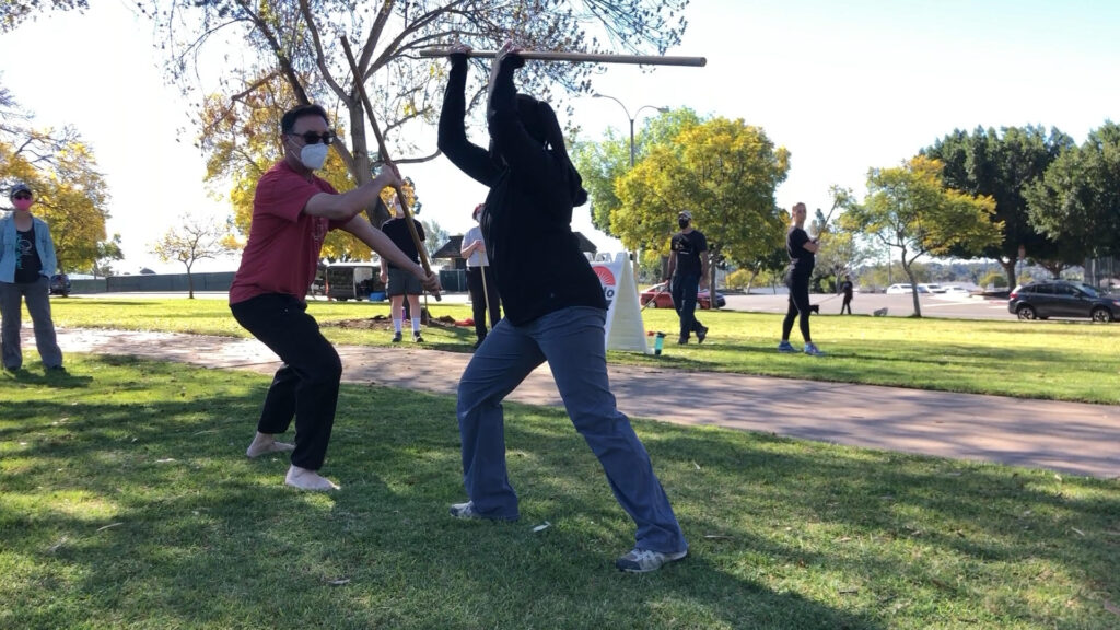 Sensei and a student demonstrating a high strike and deflection, one step of the 5th kumi jo - a partner practice with wooden staffs.