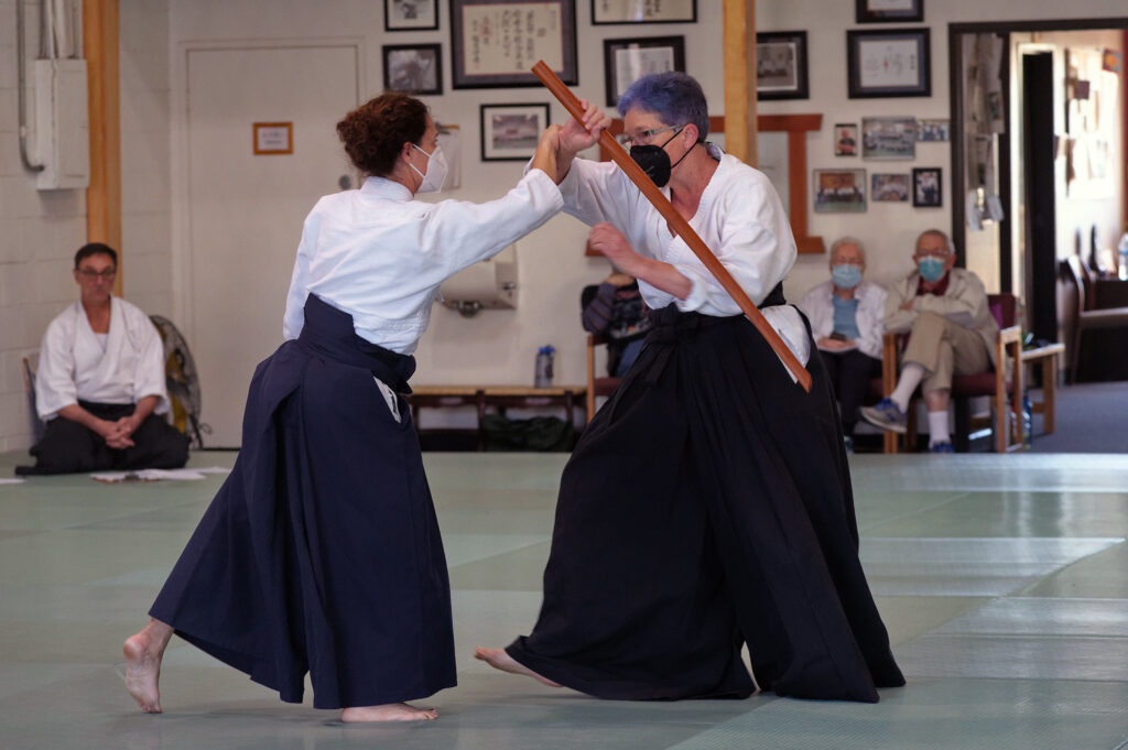 Linda raising a wooden sword in response to being grabbed by the wrist, as part of her sandan (third-degree black belt) demonstration.