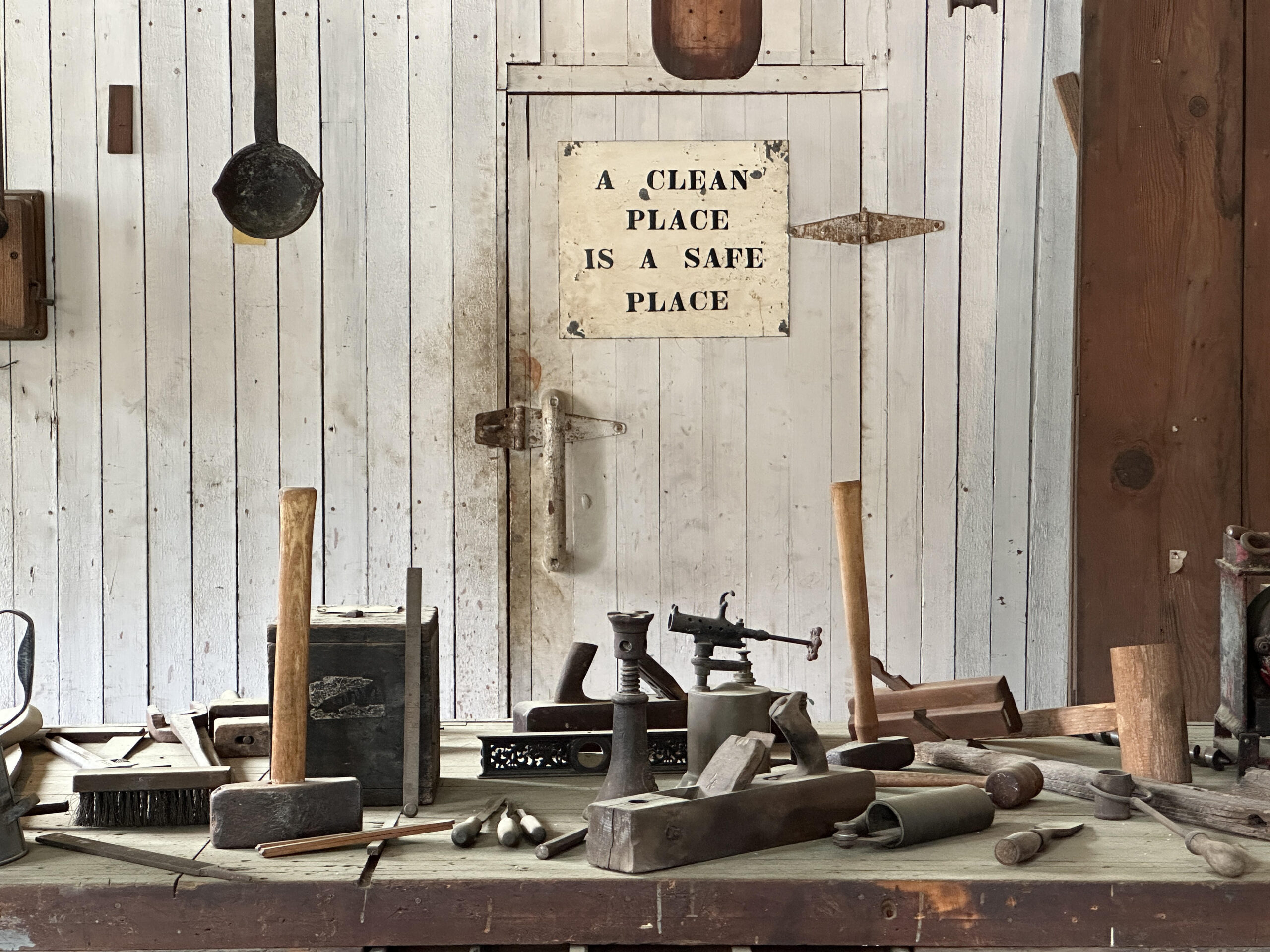 A photo of a workbench at Empire Mine State Historic Park, covered with old woodworking tools. A sign on the wall behind the workbench reads: "A Clean Place is a Safe Place."