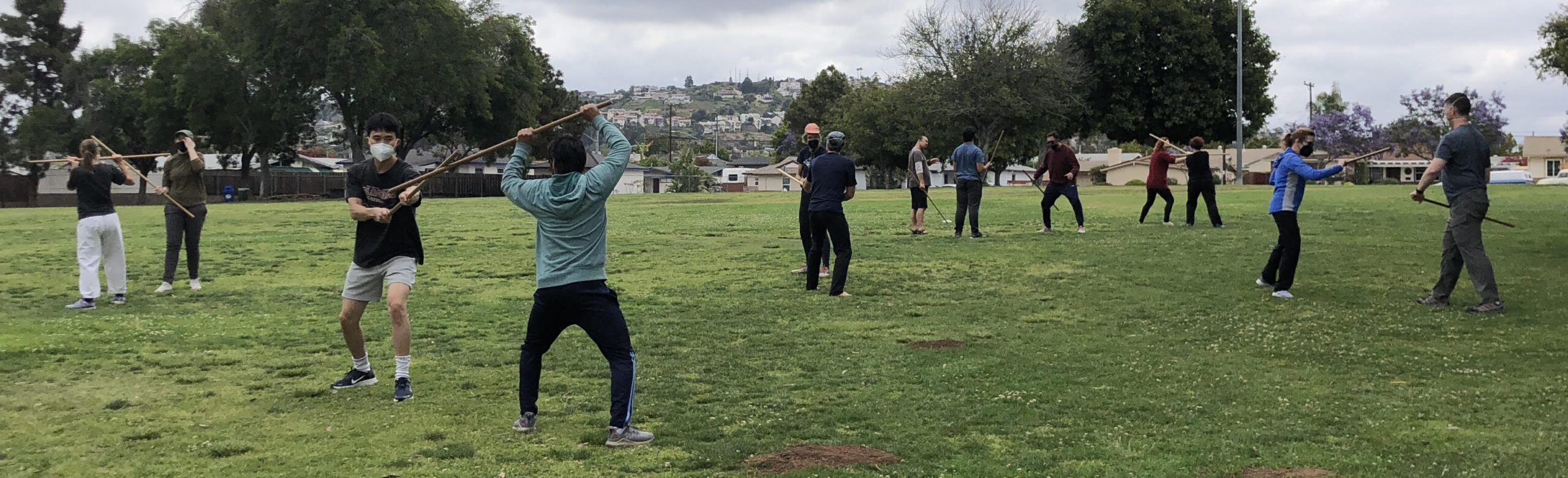 Six pairs of students from Aikido of San Diego training with the wooden staff or "jo" in the park on a cool morning.